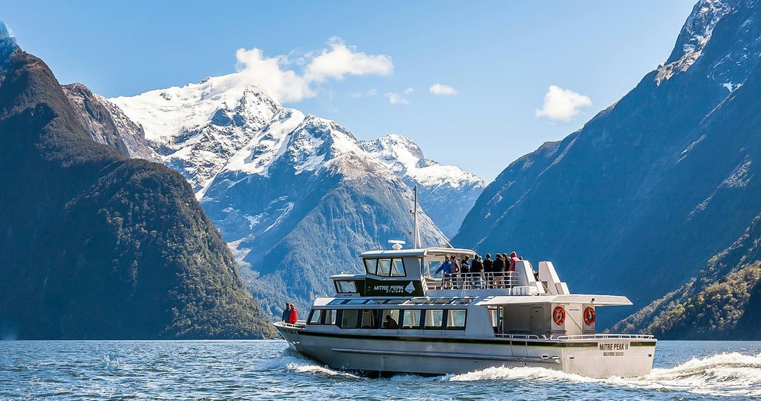 Mitre Peak rising sheer above the dark water of Milford Sound with a cruise boat below