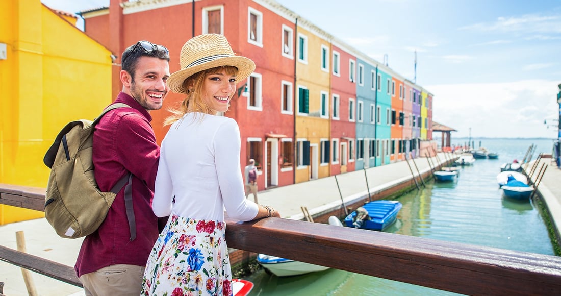 A couple looking out over a canal lined with brightly coloured houses on the island of Burano near Venice