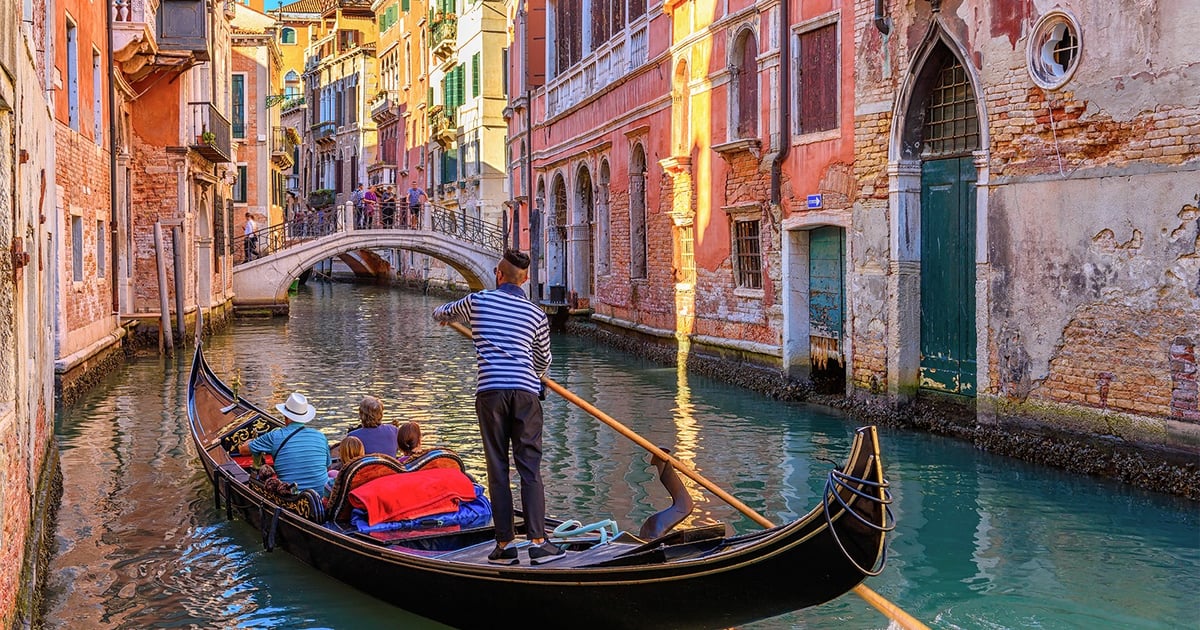 A traditional Venetian gondola with a striped-shirt gondolier gliding along a quiet canal between historic buildings in Venice