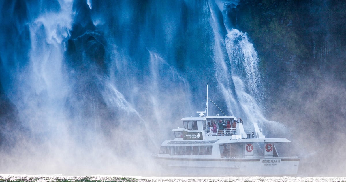 Small cruise boat sailing beneath the sheer cliffs and waterfalls of Milford Sound