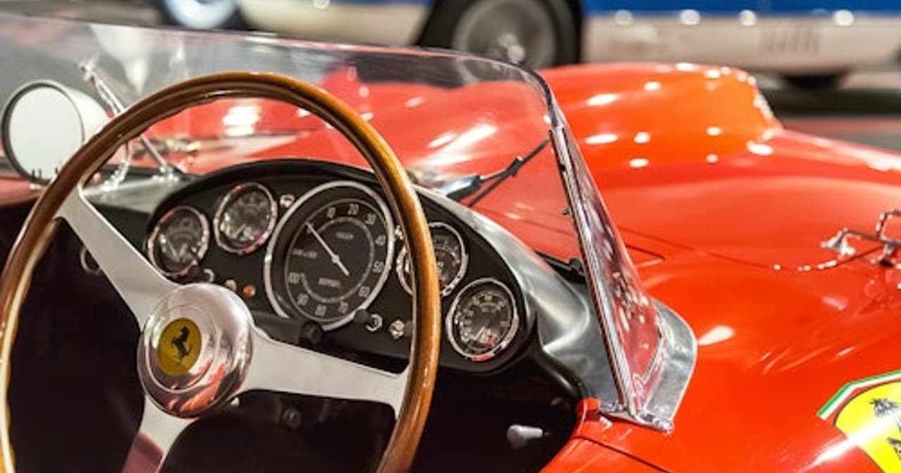 Classic red Ferrari racing car with wooden steering wheel beside a blue Ferrari at the Maranello museum