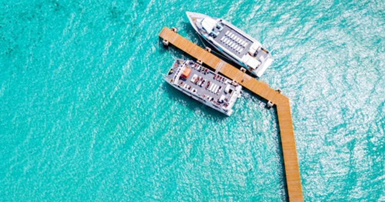 Aerial view of a wooden pier and two boats on turquoise Caribbean water at Garrafon Reef Park, Isla Mujeres