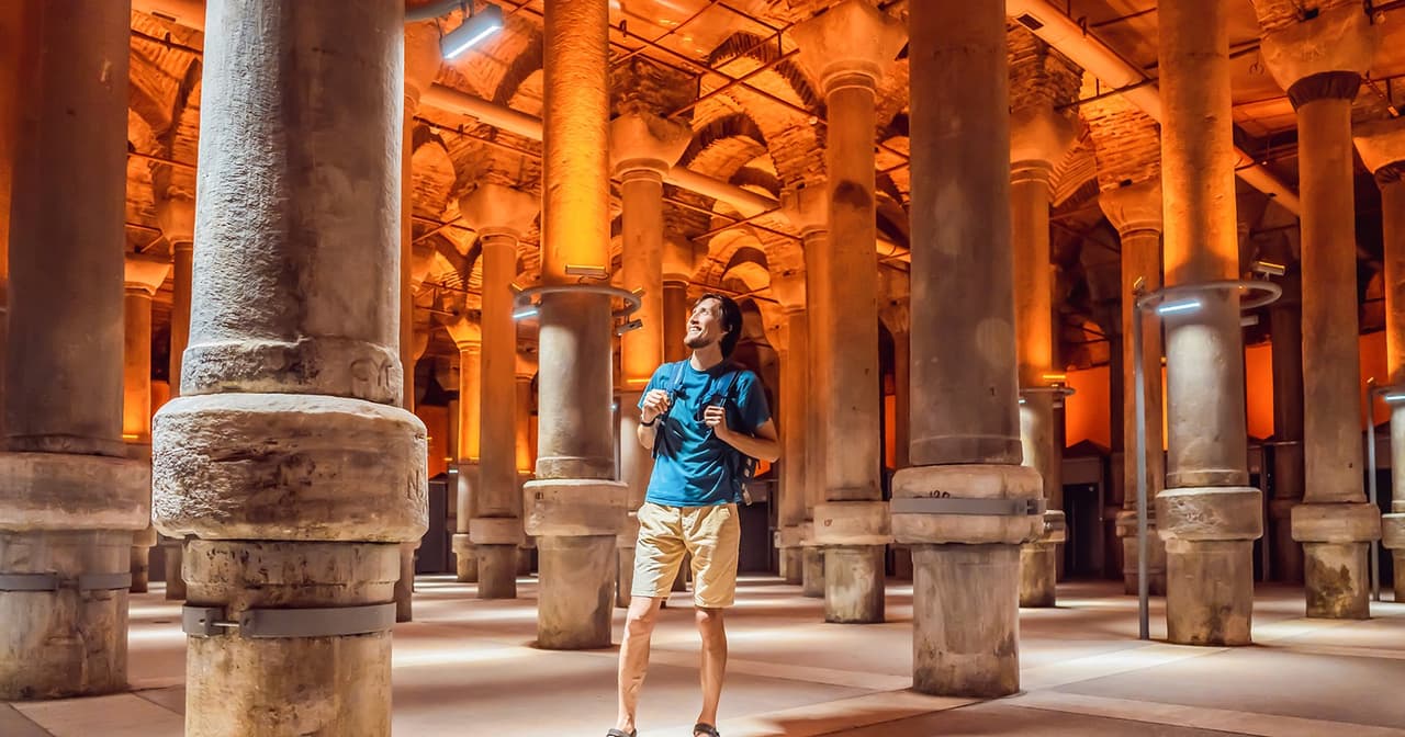 Tourist looking up among warm-lit stone columns inside the Basilica Cistern in Istanbul