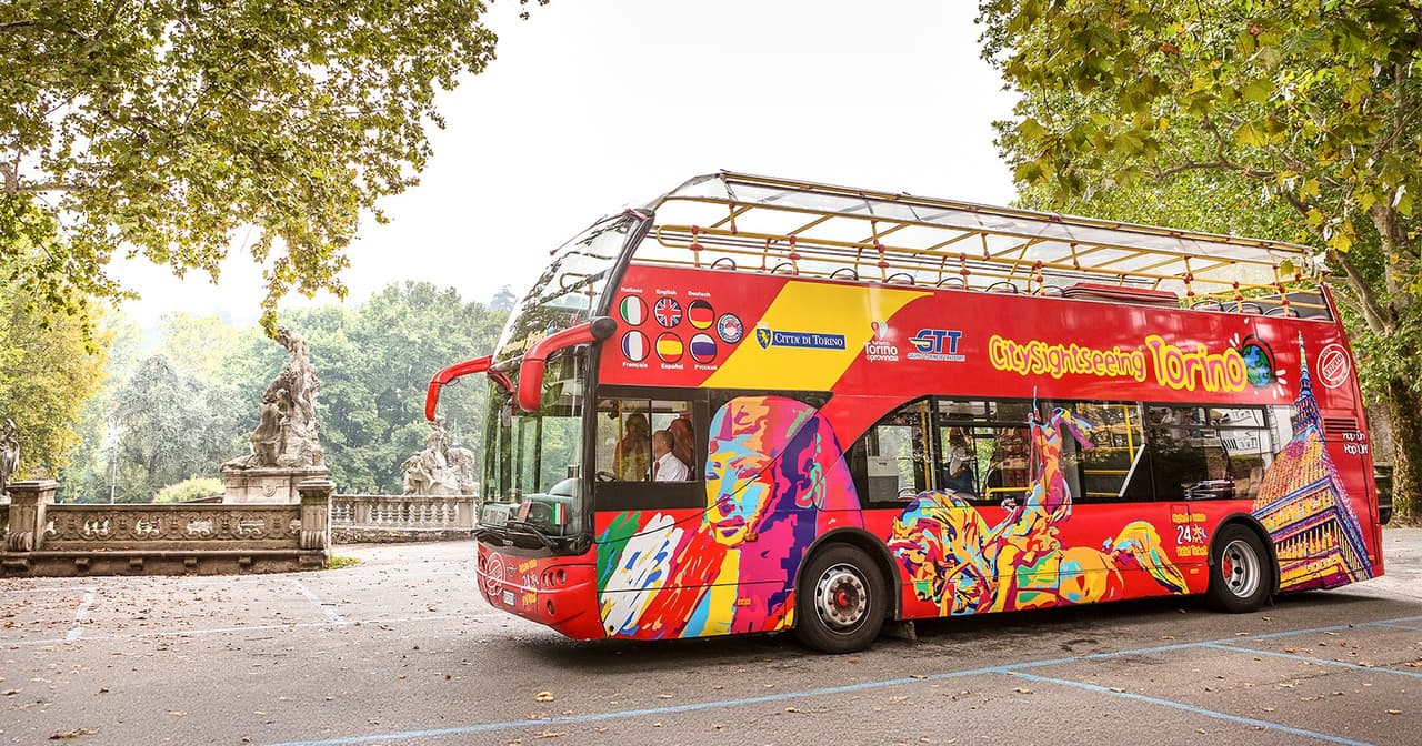Colourful open-top City Sightseeing double-decker bus on a tree-lined avenue in Turin