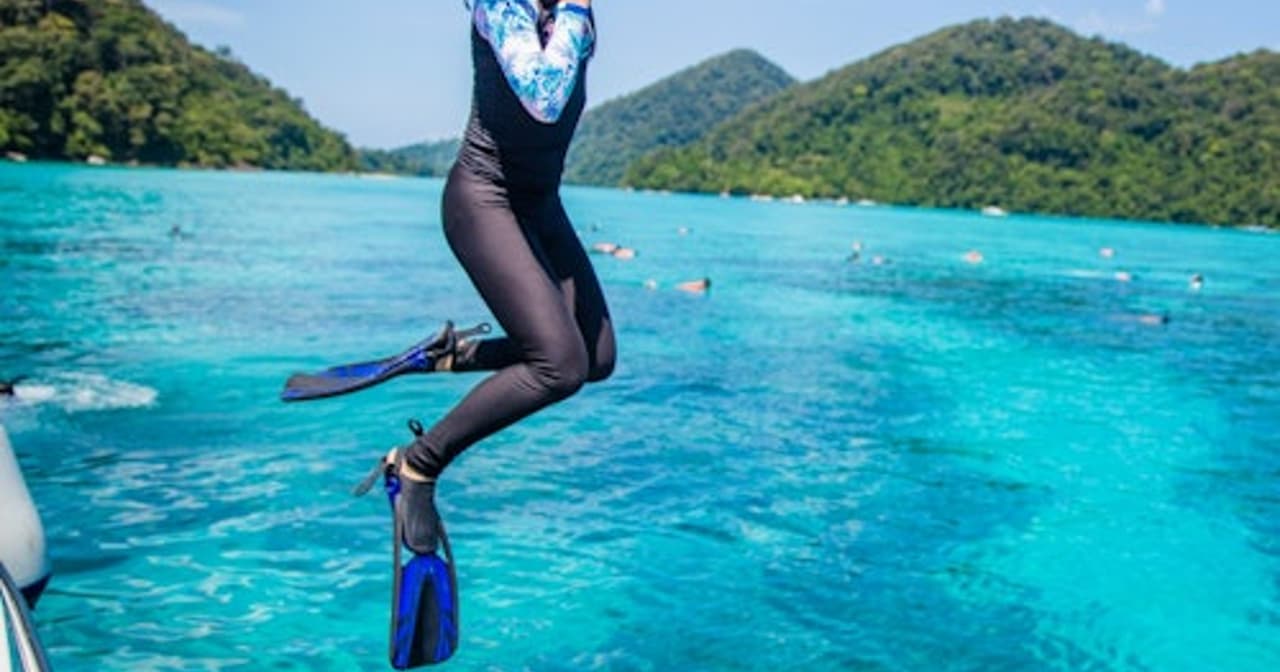 Snorkeler in a wetsuit leaping off a boat into turquoise tropical water near Khao Lak, Thailand