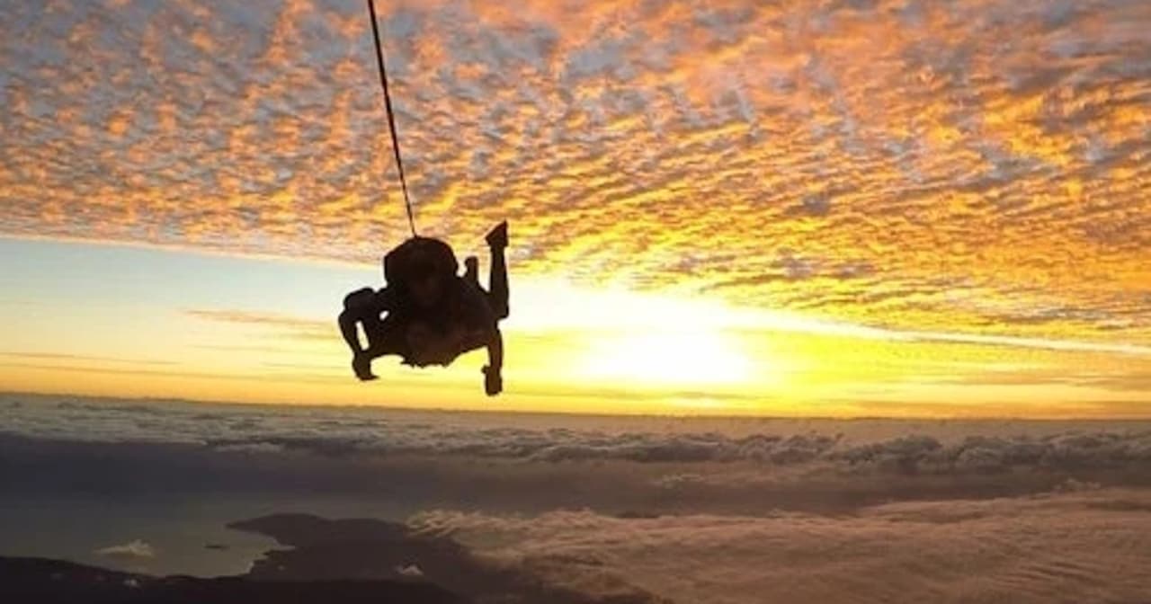 Tandem skydivers under a parachute descending through a glowing sunset sky above Cairns