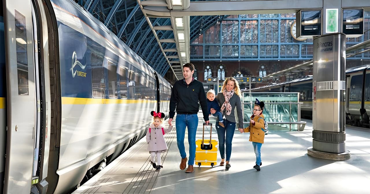 Family walking at St Pancras International station beside Eurostar train to Paris.