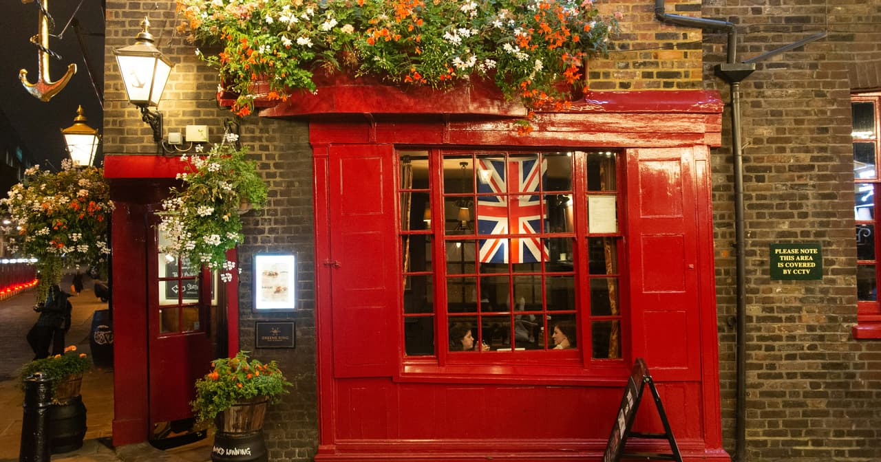 Traditional red-fronted London pub at dusk with hanging flower baskets and a Union Jack in the window