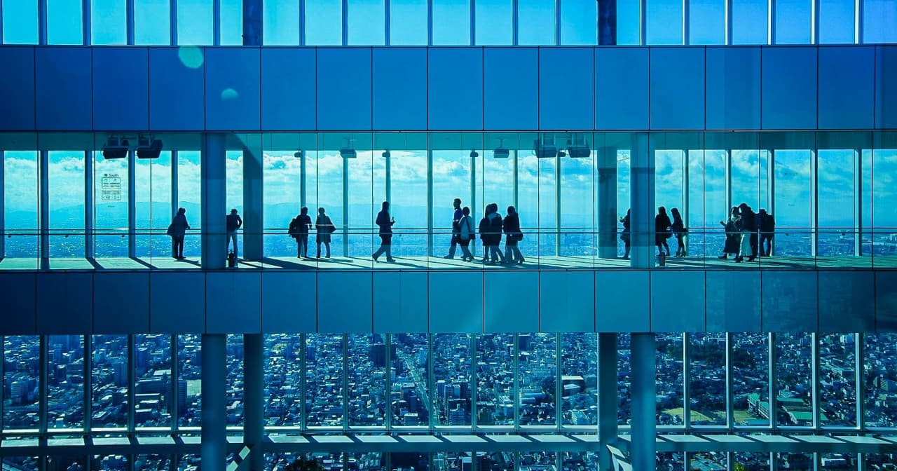 Visitors silhouetted on a high observation deck gallery overlooking the Osaka cityscape