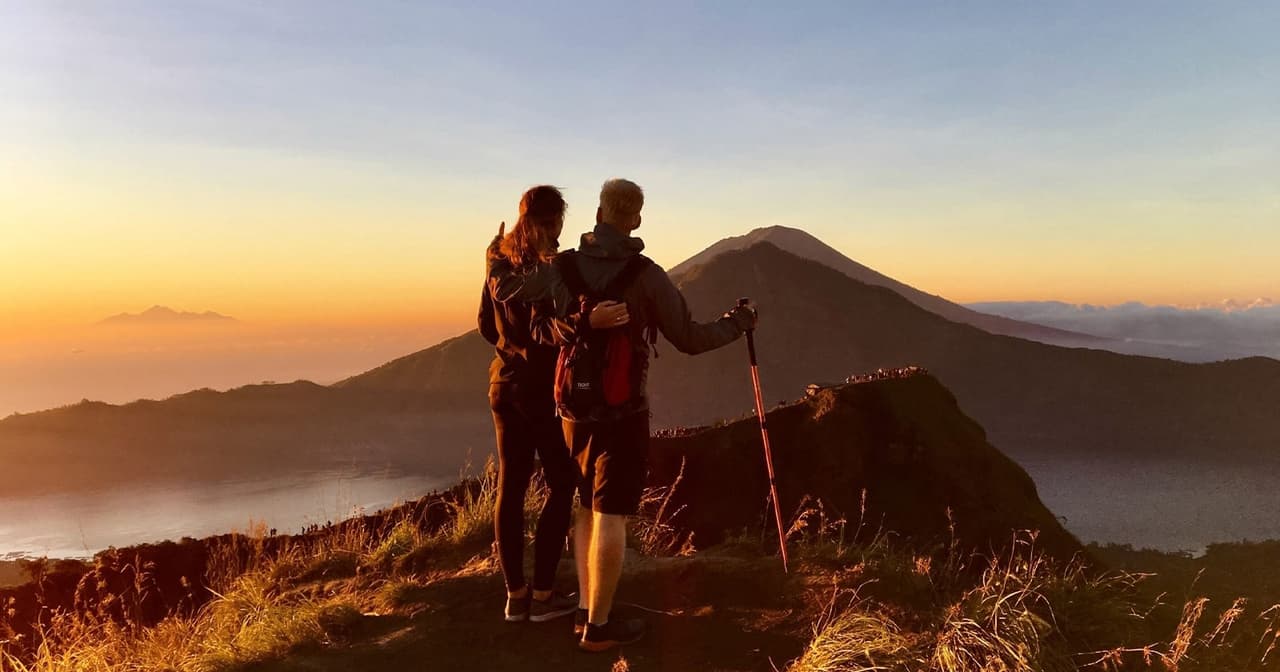 A couple at sunrise on the summit of Mount Batur looking over the volcano and crater lake in Bali