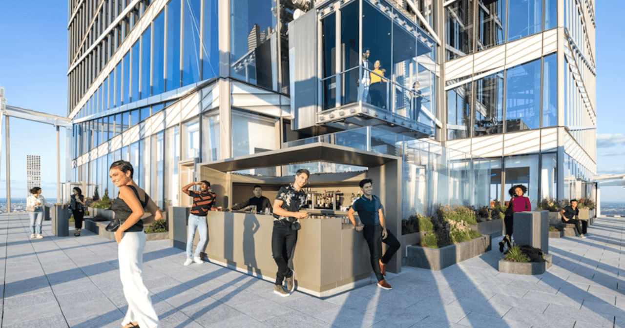 Outdoor terrace bar at Summit One Vanderbilt with guests and the glass tower above in New York