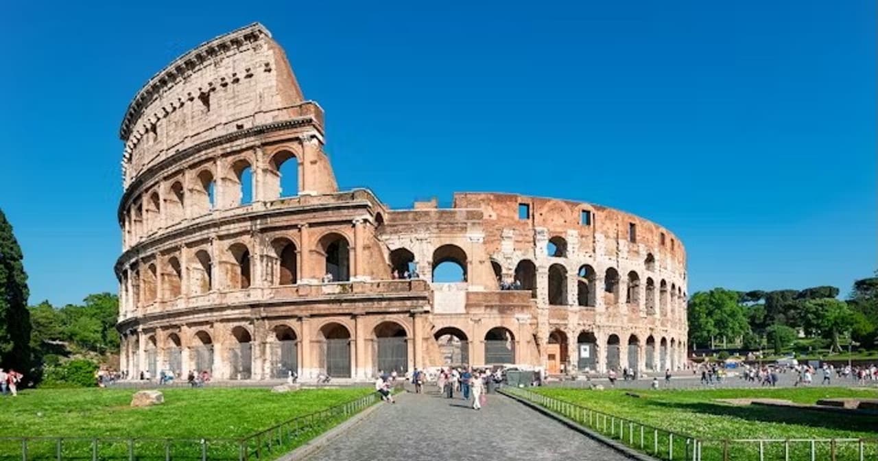 The Colosseum in Rome under a clear blue sky with a path and green lawns in the foreground