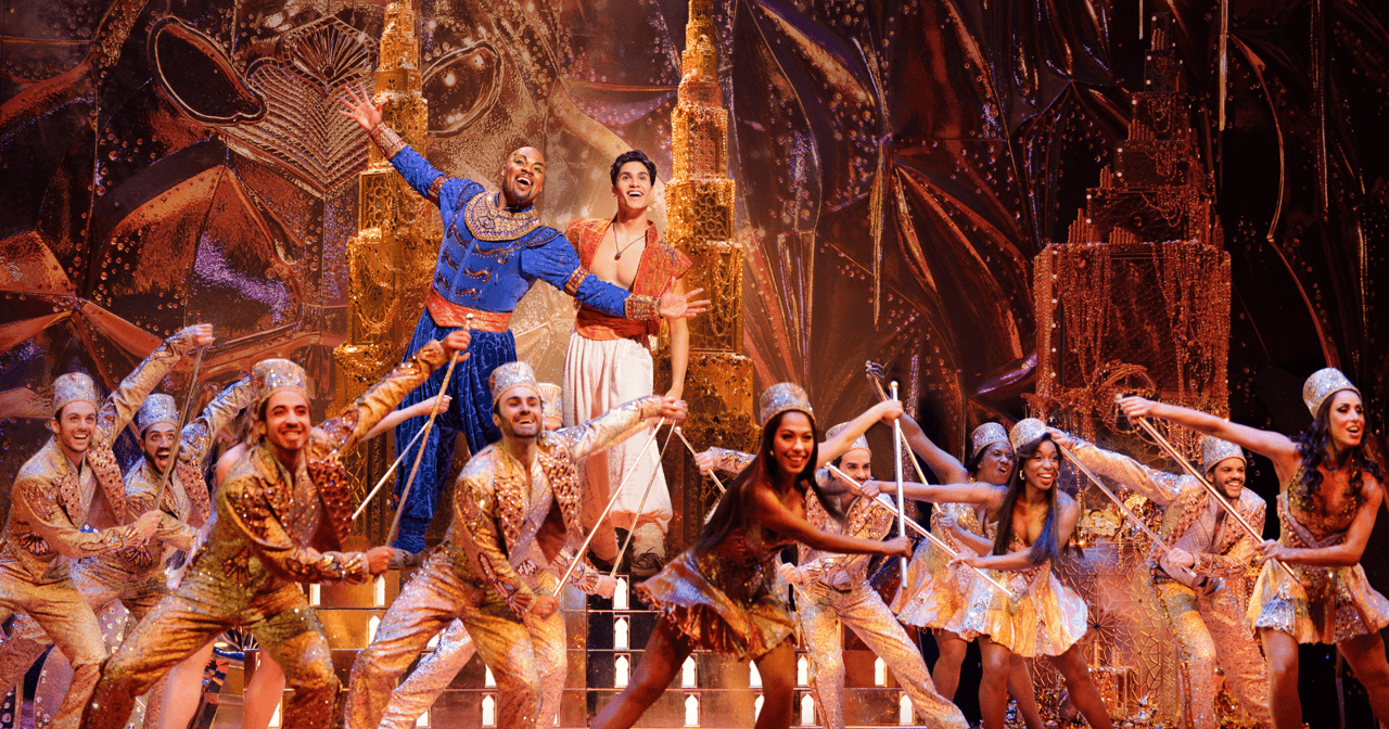 El musical de Disney Aladdin en Broadway, el Genio y Aladdin en el centro del escenario con el elenco de oro