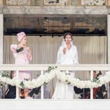 Two performers raise a toast on the balcony of the Globe stage in Much Ado About Nothing