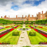 The formal gardens and Tudor brick facade of Hampton Court Palace on a summer day