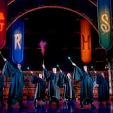 The company of Harry Potter and the Cursed Child raising lit wands beneath the Hogwarts house banners at the Palace Theatre