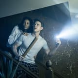 A couple on the staircase with a torch beam cutting through the dark in the London production of Paranormal Activity. Photo by Johan Persson