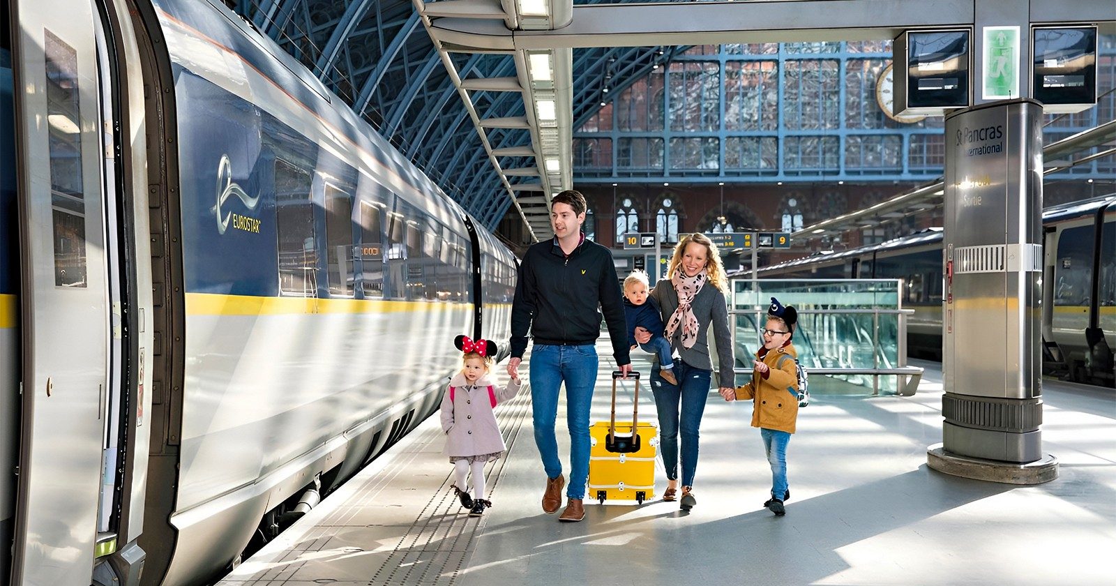 Family walking at St Pancras International station beside Eurostar train to Paris.