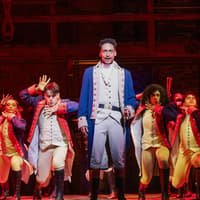 Performers in colonial costumes on stage during a Hamilton musical scene