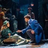 Les Misérables stage scene with actors in period costumes, one kneeling and offering a hand