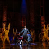 Cast performing a scene from Hamilton on stage with dramatic lighting