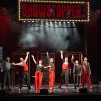 Performers on stage during Showstopper! The Improvised Musical, with arms raised in finale