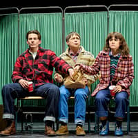 Three people sitting on stage in front of green curtains, part of "Stranger Things: The First Shadow