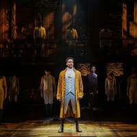 Cast performing on stage in Hamilton production, featuring lead actor in period costume