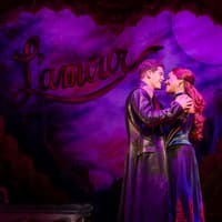 Performers embrace on stage during Moulin Rouge! The Musical in West End, with "L'amour" backdrop