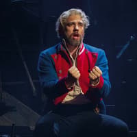Performer in Les Misérables musical scene, wearing a red and blue costume