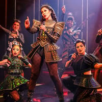 Performers in vibrant costumes on stage during the musical "Six