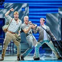 Three actors performing energetically on stage in a Mamma Mia production