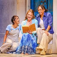 Three actors in a scene from Mamma Mia, sitting on steps with a book, in front of a blue door