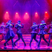 Performers on stage in vibrant costumes during the musical "Six" with dramatic lighting