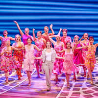Performers in colorful costumes singing and dancing in a Mamma Mia production