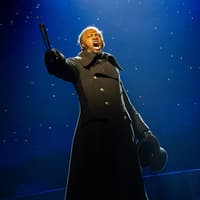 Performer on stage during Les Misérables musical, holding a hat and pointing dramatically