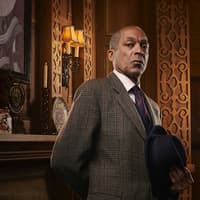 Man in a suit holding a hat, standing in an ornate room with vintage decor, related to The Mousetrap