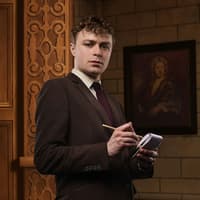 Man in suit taking notes inside a theater setting for The Mousetrap play