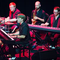 Musicians performing in Showstopper! The Improvised Musical with piano, saxophone, and drums