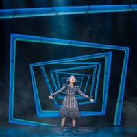Performer on stage during Beetlejuice West End show with geometric blue backdrop