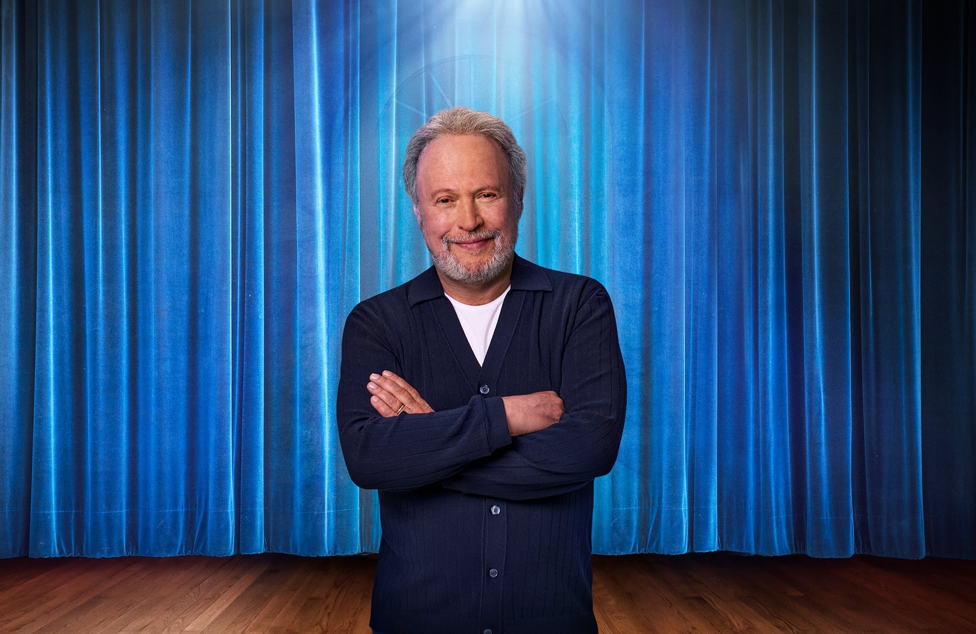 Billy Crystal, mit verschränkten Armen, steht vor einem blauen Bühnenvorhang im Schlüsselbild zu seiner Broadway-Soloshow 860