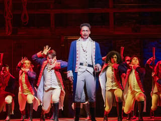 Performers in colonial costumes on stage during a Hamilton musical scene