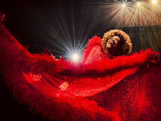Performer in vibrant red costume on stage during Kinky Boots production