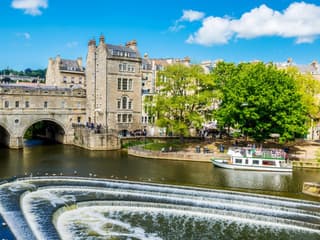 Historic Bath city street with tour group near Pulteney Bridge, live music performance nearby — Bridgerton: 1.5 Hour Guided Tour of Filming Locations in Bath with Music