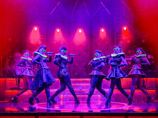 Performers on stage in vibrant costumes during the musical "Six" with dramatic lighting