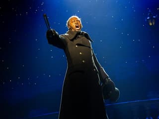 Performer on stage during Les Misérables musical, holding a hat and pointing dramatically