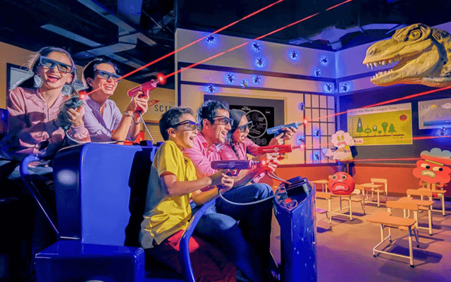 Family in 3D glasses firing laser blasters past an animatronic dinosaur on a ride at IMG Worlds of Adventure