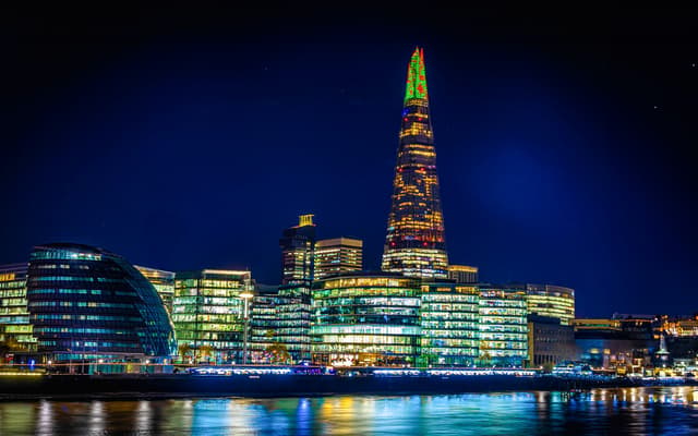 The Shard and City Hall lit up at night beside the River Thames in London with colourful reflections