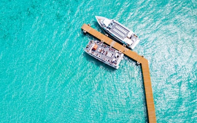 Aerial view of turquoise Caribbean water with a wooden pier and two boats at Garrafon Park, Isla Mujeres