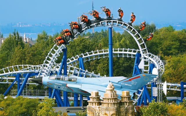 Looping roller coaster with riders at Gardaland theme park near Verona under a blue sky